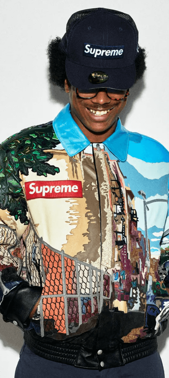 A man wearing a Supreme NYC style colorful graphic coaches jacket with a supreme box logo hat