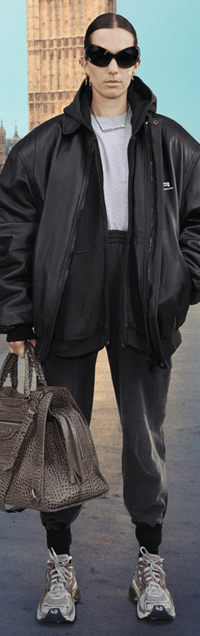 A person wearing a Balenciaga black leather sports coat, dark grey sweats, white sneakers and oversize sunglasses