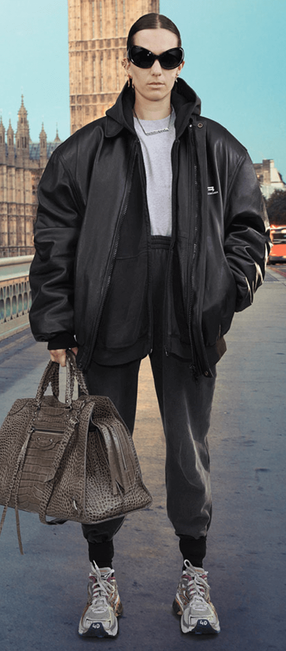 A person wearing a Balenciaga black leather sports coat, dark grey sweats, white sneakers and oversize sunglasses