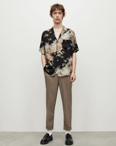 A man standing wearing an AllSaints dark floral short-sleeve button up with beige pants