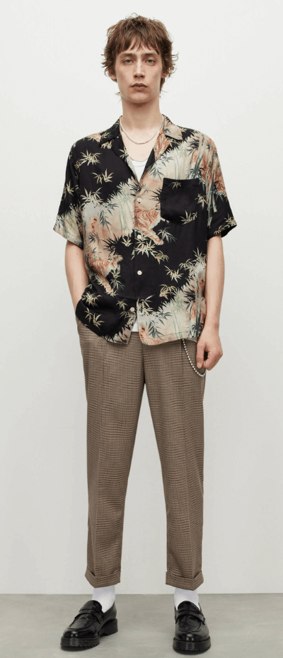 A man standing wearing an AllSaints dark floral short-sleeve button up with beige pants