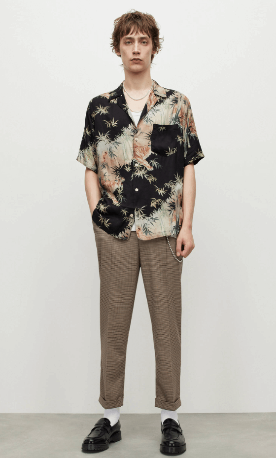 A man standing wearing an AllSaints dark floral short-sleeve button up with beige pants