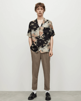 A man standing wearing an AllSaints dark floral short-sleeve button up with beige pants