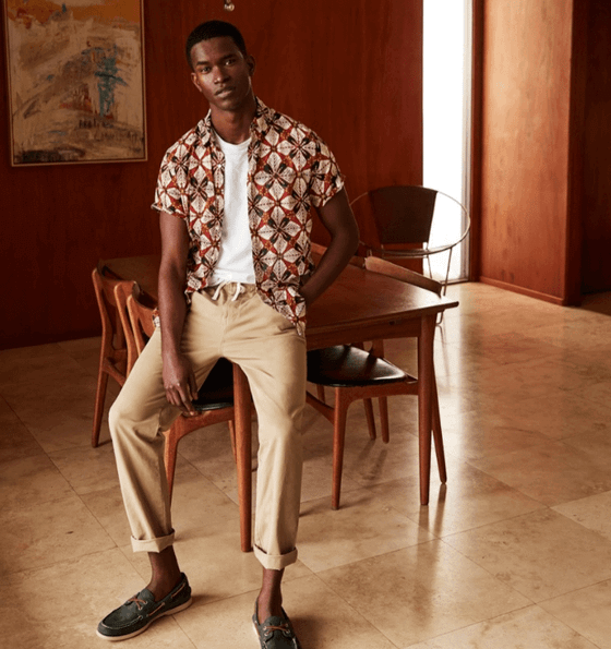 A man wearing a patterned J Crew short-sleeve button up with rolled up beige khakis and boat shoes
