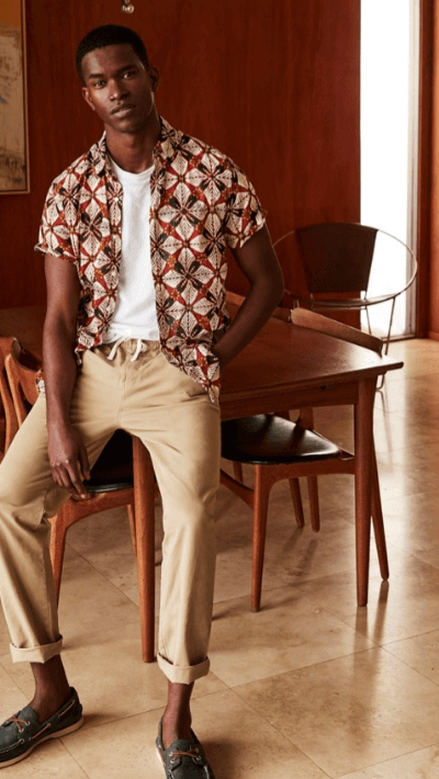 A man wearing a patterned J Crew short-sleeve button up with rolled up beige khakis and boat shoes