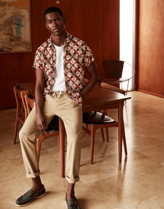 A man wearing a patterned J Crew short-sleeve button up with rolled up beige khakis and boat shoes