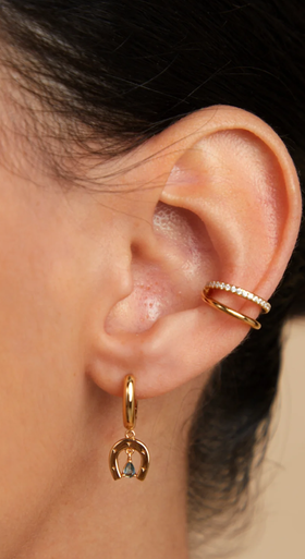A woman wearing Astrid & Miyu horseshoe charm huggies in gold