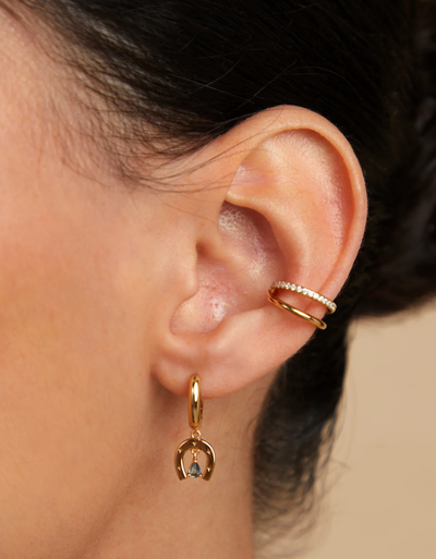 A woman wearing Astrid & Miyu horseshoe charm huggies in gold
