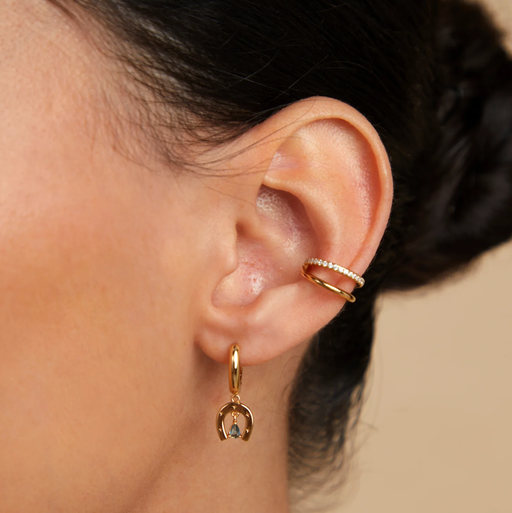 A woman wearing Astrid & Miyu horseshoe charm huggies in gold