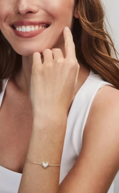 A woman wearing Kendra Scott ari heart gold delicate chain bracelet in bubblegum pink