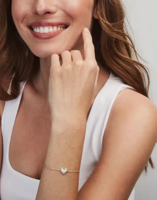 A woman wearing Kendra Scott ari heart gold delicate chain bracelet in bubblegum pink