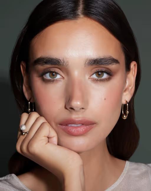 A woman wearing Strathberry​ crescent hoop earrings - 22 carat gold gilded
