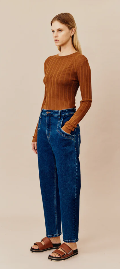 A woman wearing a dark orange Ginger and Smart shirt with blue jeans