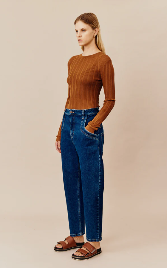 A woman wearing a dark orange Ginger and Smart shirt with blue jeans