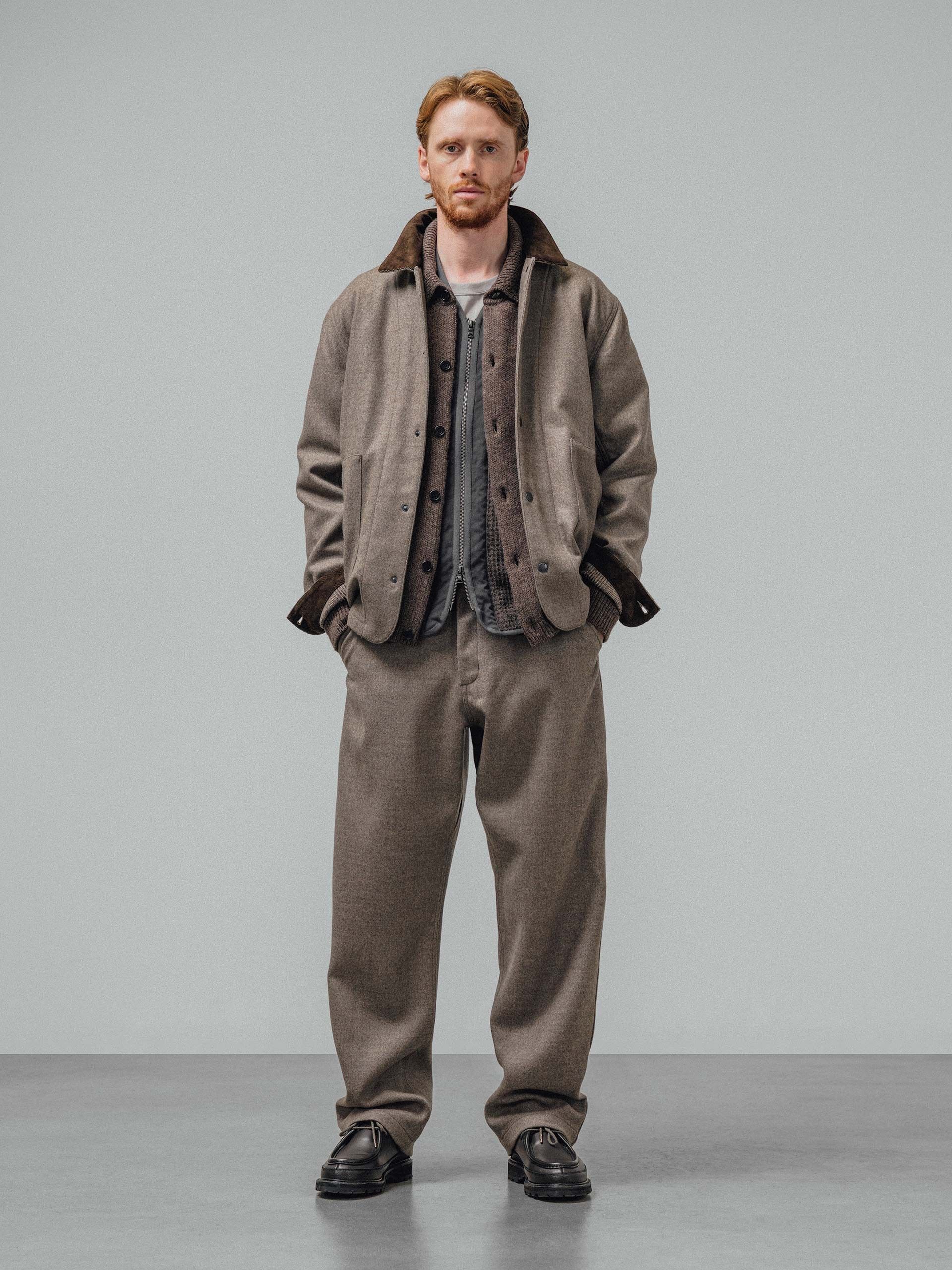 A model in a light brown jacket with a dark corduroy collar over a cardigan and zip liner, with matching wide trousers