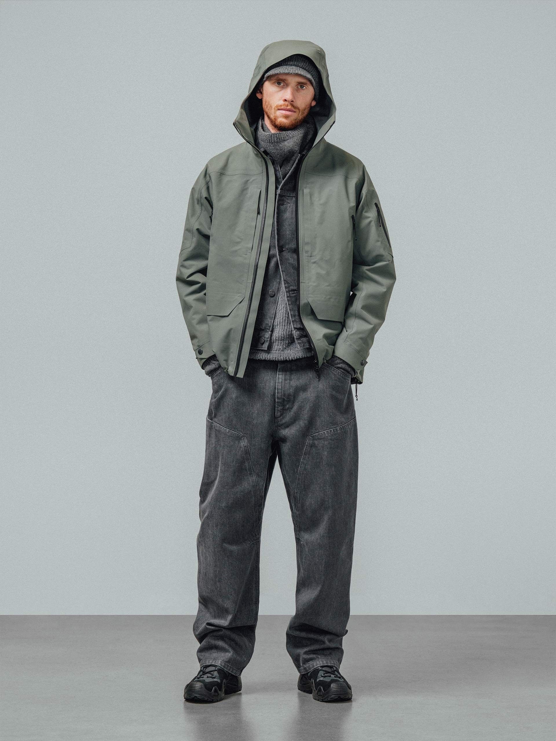 A model in a hooded green shell jacket over grey knitwear and washed grey jeans