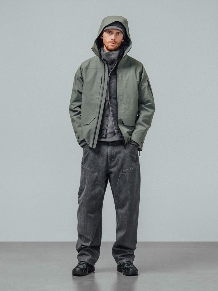 A model in a hooded green shell jacket over grey knitwear and washed grey jeans
