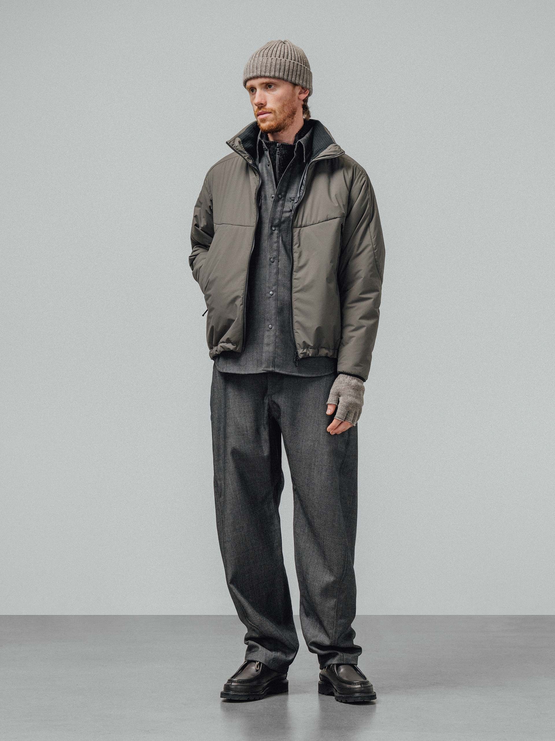 A model in a stone-grey insulated jacket over a grey shirt and wide grey trousers