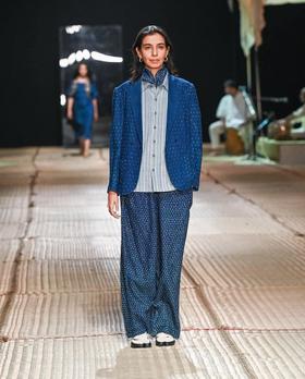 A woman wearing an indigo hand-woven 11.11 / eleven eleven jacket and wide-leg trousers