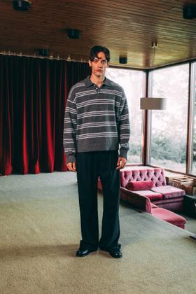 A man wearing a grey striped 33mm knitted polo jumper and black wide-leg trousers