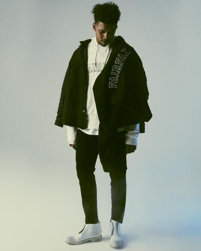 A man wearing a black 424 Fairfax overshirt layered over a white FAIRFAX hoodie with black trousers and white boots