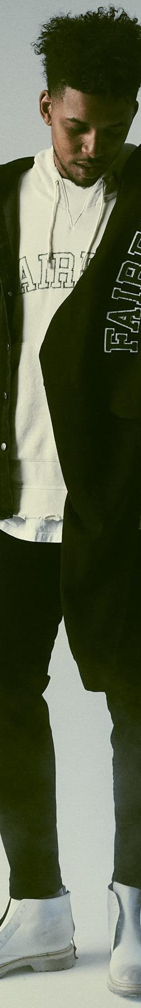 A man wearing a black 424 Fairfax overshirt layered over a white FAIRFAX hoodie with black trousers and white boots