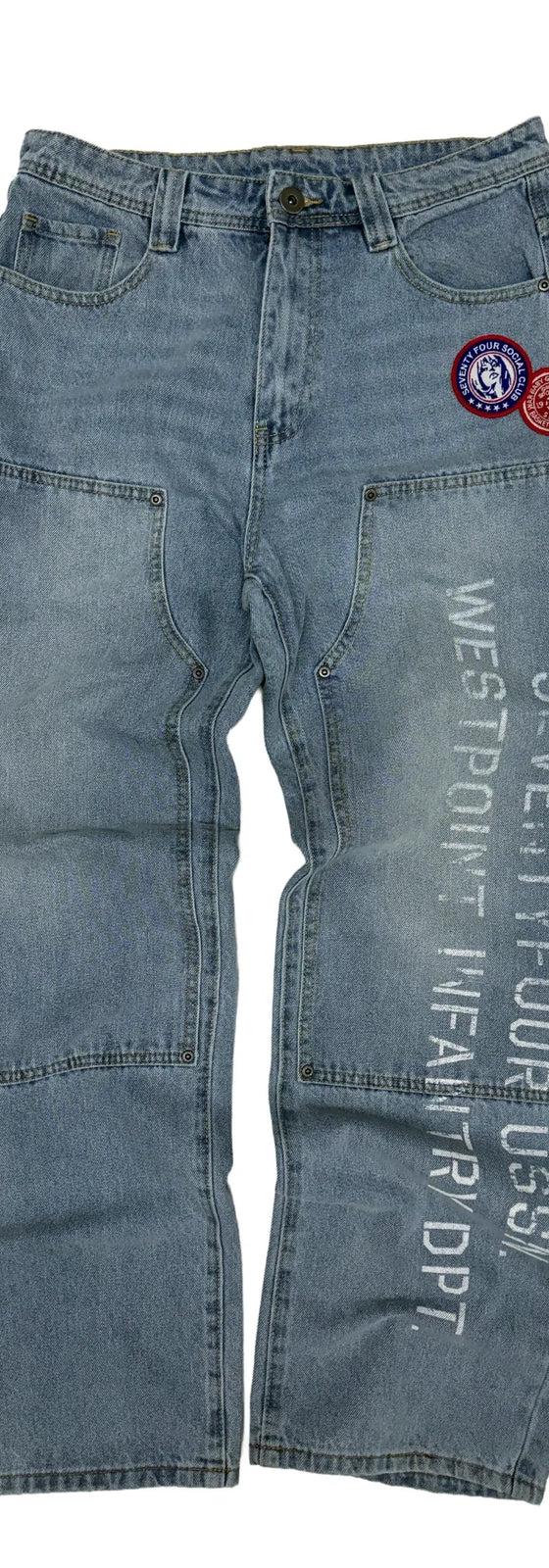 A pair of stonewashed 74isWar carpenter jeans with military patches and stenciled lettering