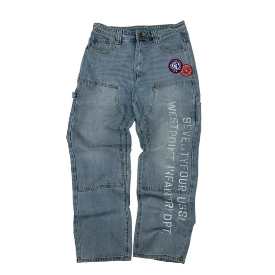 A pair of stonewashed 74isWar carpenter jeans with military patches and stenciled lettering