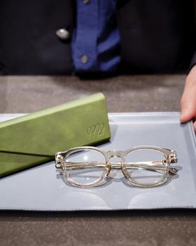 A pair of clear 999.9 optical frames on a shop tray beside a green case