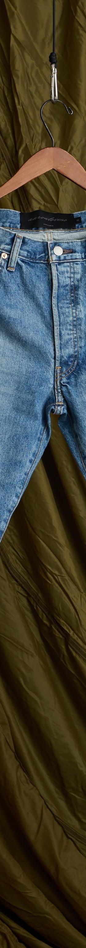 A pair of faded light-wash Aaron Levine jeans hanging against an olive canvas backdrop