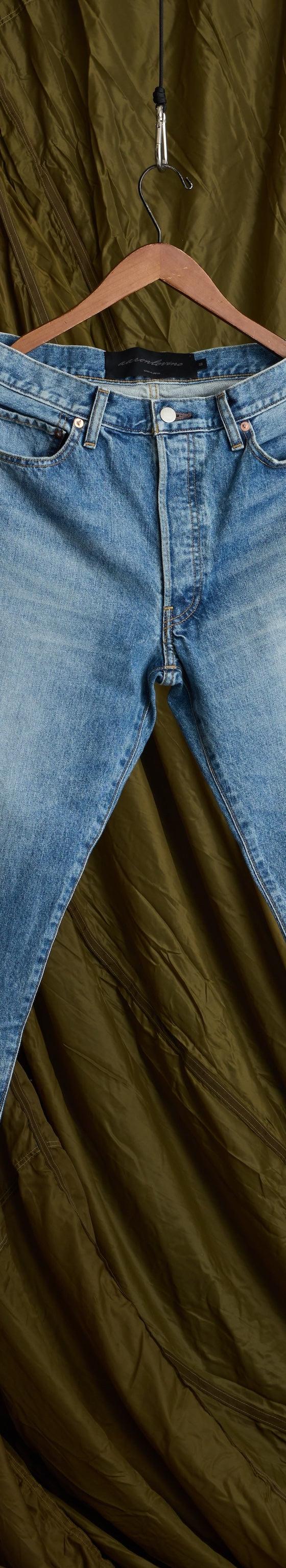 A pair of faded light-wash Aaron Levine jeans hanging against an olive canvas backdrop