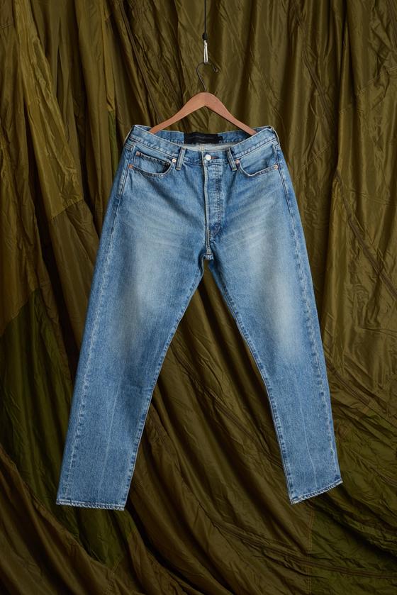 A pair of faded light-wash Aaron Levine jeans hanging against an olive canvas backdrop