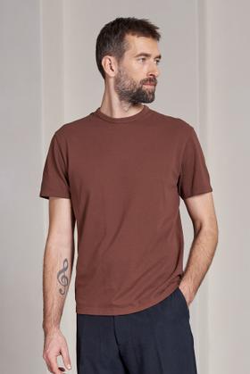 A man wearing a brown About Companions T-shirt with navy trousers