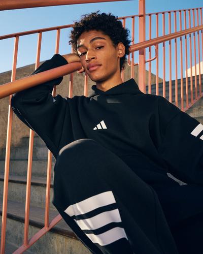 A man in a black adidas hoodie and three-stripe track pants sitting on concrete steps
