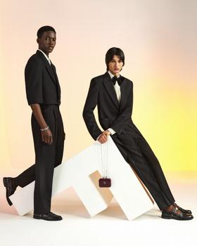 Two models in black tailored suiting posing against a warm gradient backdrop
