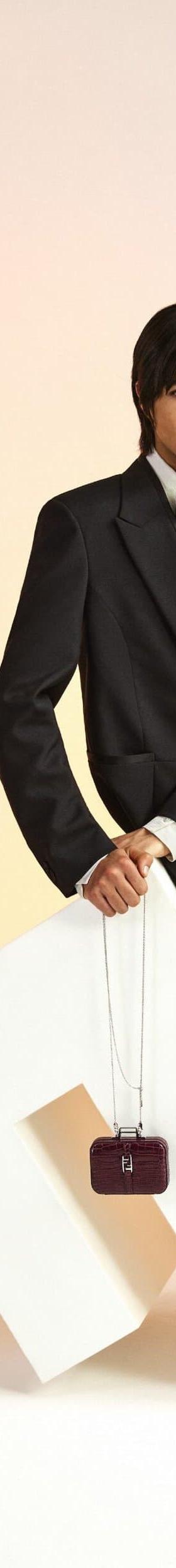 Two models in black tailored suiting posing against a warm gradient backdrop