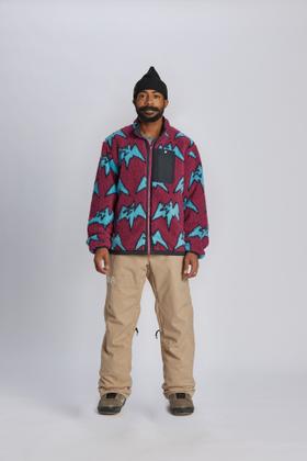 A man wearing a magenta and blue mountain-print Airblaster fleece jacket with tan snowboard pants
