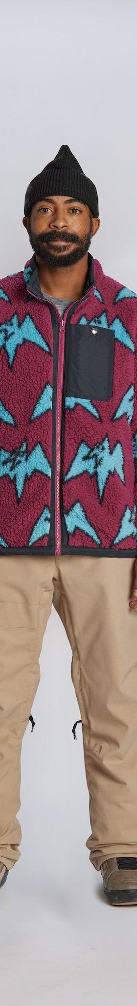 A man wearing a magenta and blue mountain-print Airblaster fleece jacket with tan snowboard pants