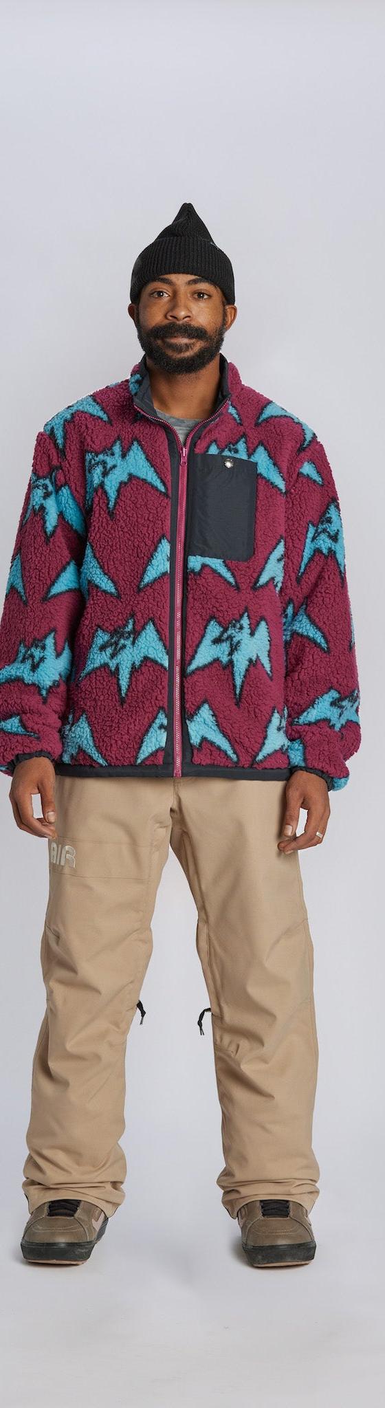 A man wearing a magenta and blue mountain-print Airblaster fleece jacket with tan snowboard pants