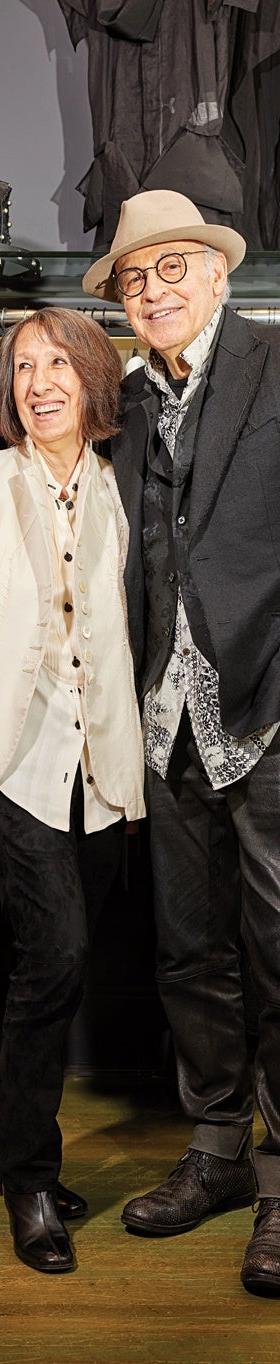 A couple wearing an ivory Alan Bilzerian jacket and a black blazer with leather trousers inside the boutique
