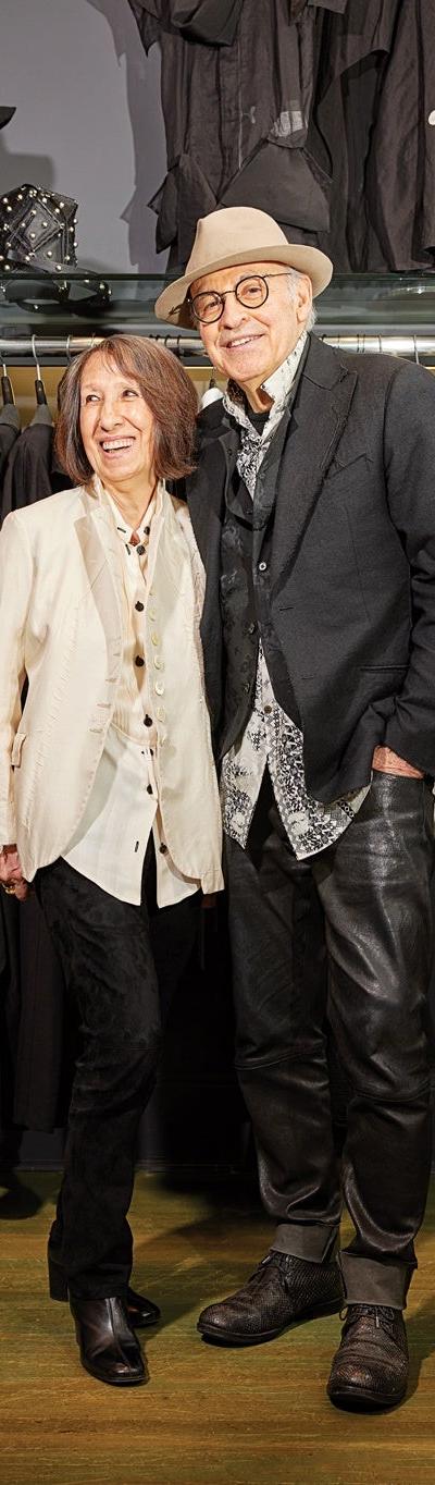 A couple wearing an ivory Alan Bilzerian jacket and a black blazer with leather trousers inside the boutique