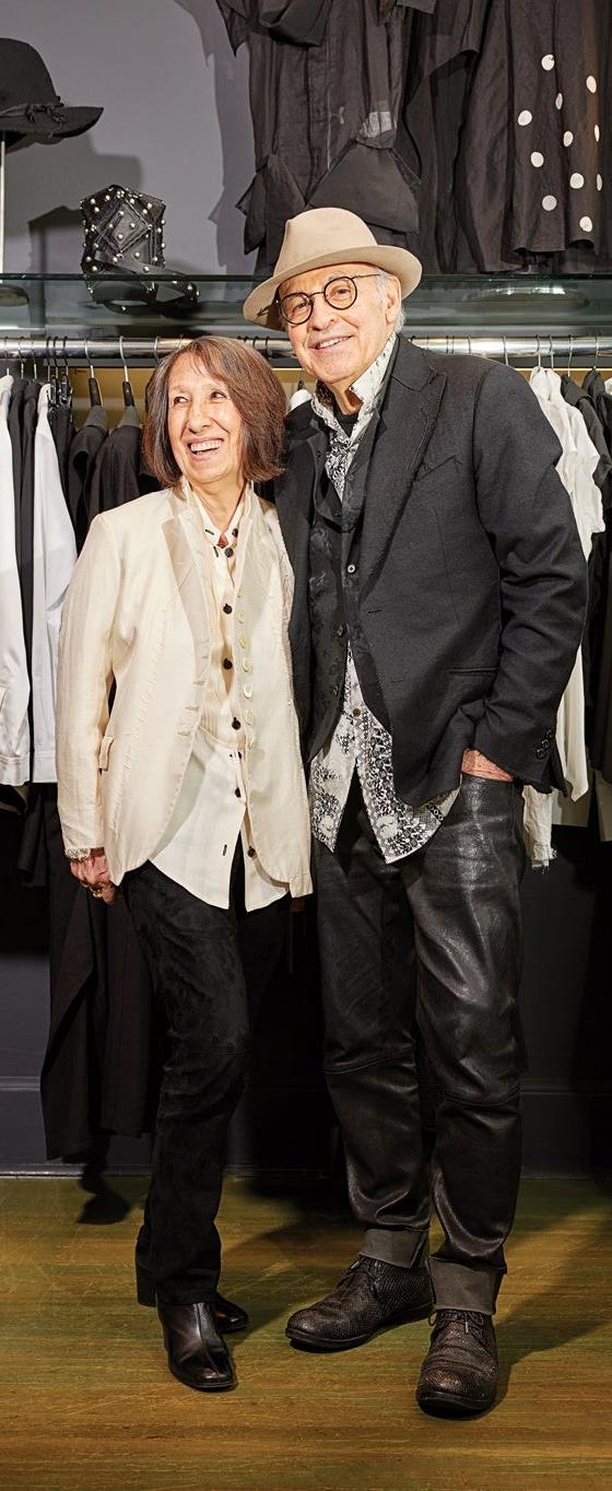 A couple wearing an ivory Alan Bilzerian jacket and a black blazer with leather trousers inside the boutique