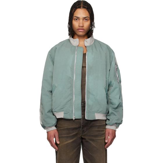 A man wearing a green Alexander DiGenova bomber jacket with faded brown jeans