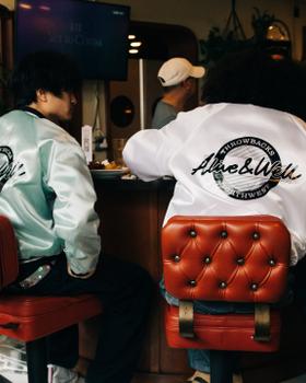 Two people seated at a diner counter wearing Alive & Well satin coach jackets