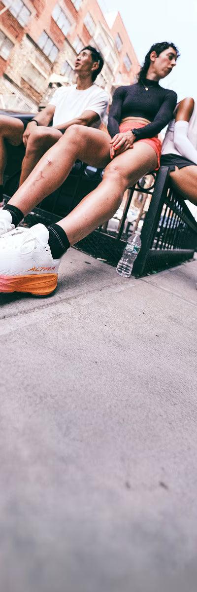 Three runners in Altra road running shoes sitting on a city street railing