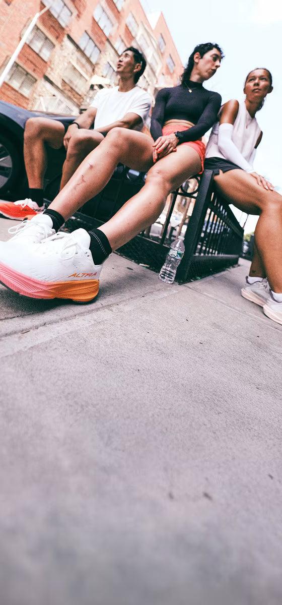 Three runners in Altra road running shoes sitting on a city street railing