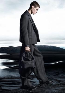 A man in a grey wool suit carrying a black leather drawstring bag