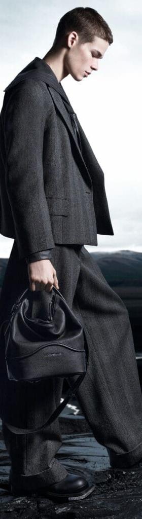 A man in a grey wool suit carrying a black leather drawstring bag