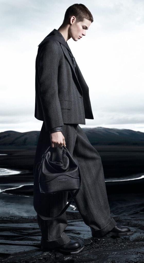 A man in a grey wool suit carrying a black leather drawstring bag
