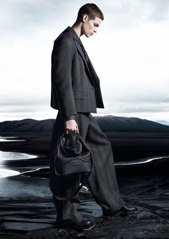 A man in a grey wool suit carrying a black leather drawstring bag